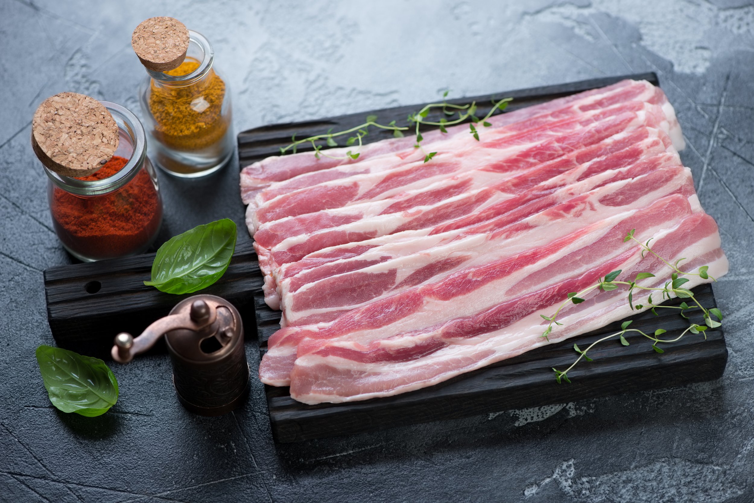 Black wooden chopping board with raw fresh bacon on a grey concrete background Image placeholder indicating a photo is needed, typically used in web design or content management systems to signal missing visual content.